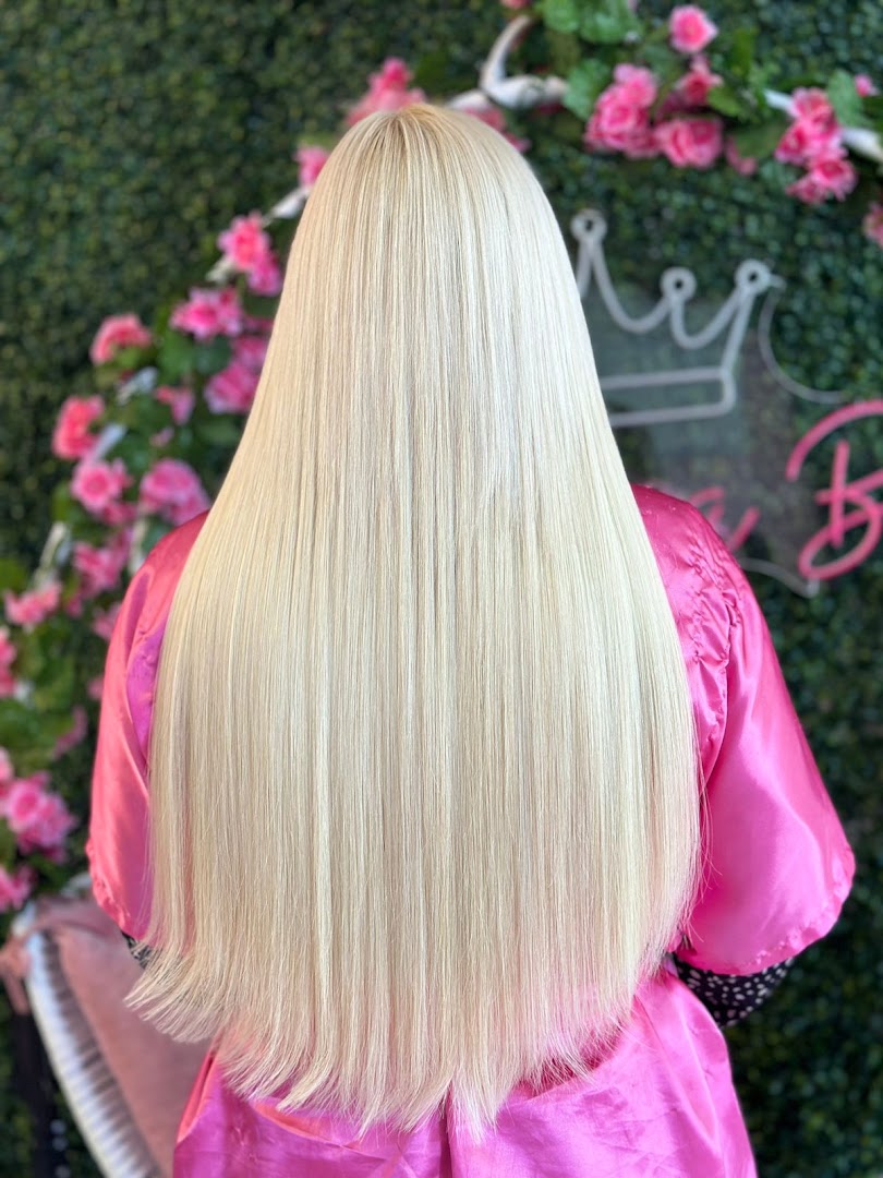 Cabelo loiro platinado e liso, cliente de roupão rosa em frente a painel de flores