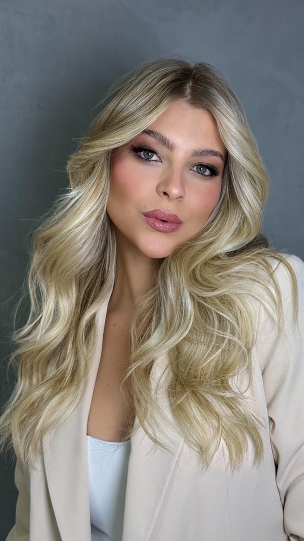 Cliente de perfil com cabelo loiro em ondas, blusa rosa e fundo de flores no salão